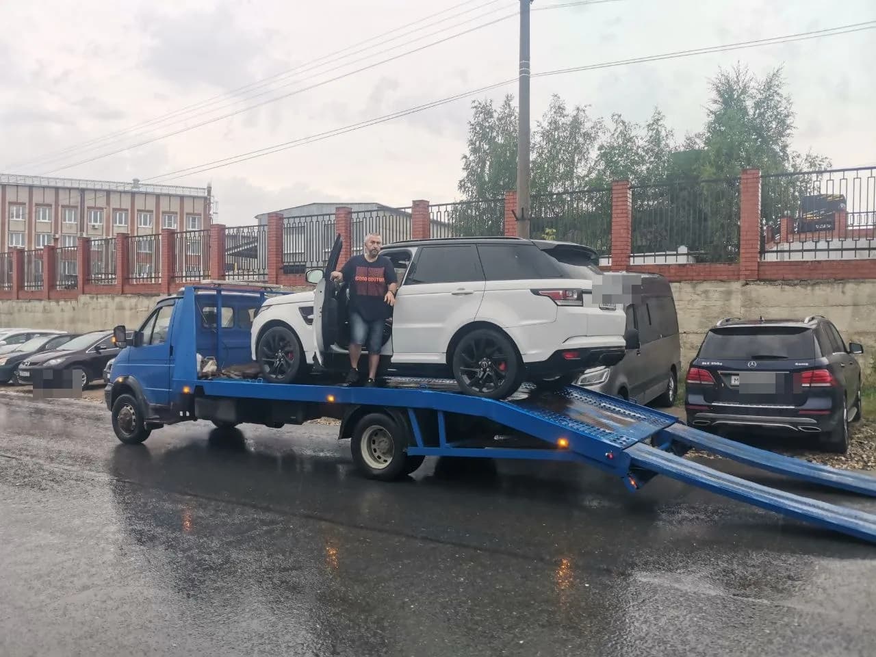 Давид рядом с белым внедорожником Range Rover на синем эвакуаторе